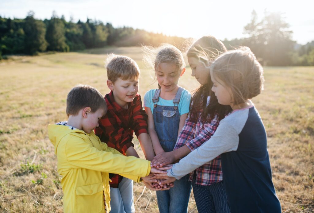 Group of children standing on field trip in nature, putting hands together